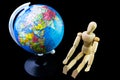 Wooden figure sitting besidea globe model. Royalty Free Stock Photo