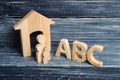 Wooden figures of children stand in a row from small to large near the letters of the English alphabet abc.