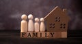 Wooden figures family standing beside a wooden house on a wooden cube that writes the word family. The concept of Protection and