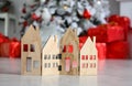 Wooden figures of houses stand on the floor against the background of a Christmas tree and gifts. Royalty Free Stock Photo