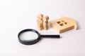 Wooden figures of people are standing near a wooden house and a magnifying glass. The concept of home search, buying and selling.