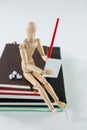 Wooden figurine sitting on a pile of books writing on a paper Royalty Free Stock Photo