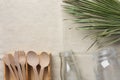 Wooden flatware cutlery crystal jar bottle green palm leaf on linen fabric background. Plastic-free alternatives zero waste