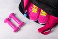 On the wooden floor sports bag with pink things in it uncovered, and two dumbbells