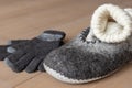 On the wooden floor there are a men's slippers made of dried wool, a handmade woolen sock and gloves in natural