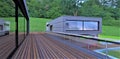 Wooden flooring on the terrace with glass railing. Large sliding windows reflect the environment. 3d rendering