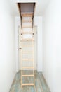 Wooden foldable pull up attic stairs ladder at empty white home corridor.