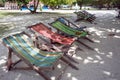 Wooden folding chaise lounges stand in the shade of trees on the street of a tourist resort