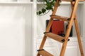 Wooden folding ladder near white shelving unit indoors