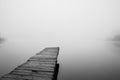 Wooden footbridge on lake with thick mist foggy air over water. Early chilly morning in late autumn. Peaceful atmosphere in nature