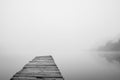 Wooden footbridge on lake with thick mist foggy air over water. Early chilly morning in late autumn. Peaceful atmosphere in nature