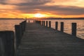 Wooden footbridge with pilings at sunset on Lake Neusiedl. The orange sun reflects in the waves of the water. The cloudy sky makes Royalty Free Stock Photo