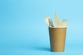 Wooden forks, knives and spoons for food in a paper cup on a colored background. Eco-friendly disposable tableware without plastic Royalty Free Stock Photo