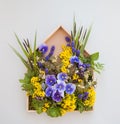 A wooden frame in the form of a house in which is decorated with flowers, pansies and other yellow and purple wildflowers