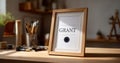Close-up of a wooden framed certificate with the word grant on a desk surrounded by art supplies and natural light in a cozy Royalty Free Stock Photo
