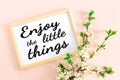 Wooden frame with the inscription Enjoy the little things, spring inspirational and motivational text and floral cherry branches