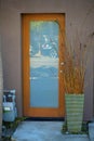 Wooden front door with glass pannel and entryway dry plant in green vase or pot with cement walkway and brown wall Royalty Free Stock Photo