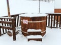 Wooden furaco baptismal font strewn with snow stands on a terrace with a wooden fence on a snowy winter day