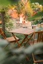 Wooden furniture in the garden against the backdrop of a fire on the patio. Among the branches of the bush stands a wooden table Royalty Free Stock Photo