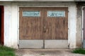 Wooden garage doors made of dilapidated boards with painted windows and metal rain protection mounted on cracked wall Royalty Free Stock Photo