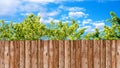 Wooden garden fence at backyard, green trees and blue sky with white clouds Royalty Free Stock Photo