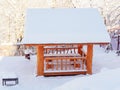 A wooden gazebo covered with snow stands on a snow-covered meadow among trees