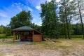 Wooden gazebo next to a clearing full of yellow and green grass and with a few trees by the river