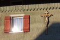 wooden green facade with crucifix and red color shutter of bavarian farmhouse