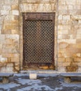 Wooden grunge window with decorated iron grid over stone bricks wall and two marble garden benches