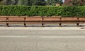 Wooden guardrail on concrete sidewalk. Fence made of brick with hedge on behind and street in front