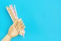 Wooden hand hold drinking paper straws for party with golden, white, pink stripes on blue background Royalty Free Stock Photo