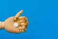 A wooden hand holds out a classic medical white pill with a score on a traditional blue background. Selective focus