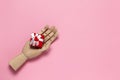 Wooden hand holds small red gift box with white bow and little heart on pink background, copy space, flat lay. March 8, February Royalty Free Stock Photo