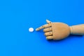 Wooden hand points to a classic medical white pill with a score on a traditional blue background. Selective focus