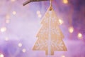 Wooden handmade Christmas tree ornament hanging on branch. Shining garland golden lights. Purple background. Magical atmosphere. Royalty Free Stock Photo