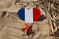 wooden handmade heart in the colors of flag of France blue, white and red with red starfish in golden sand on beach