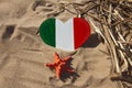 Wooden handmade heart in the colors of flag of Italy green, white and red with red starfish in golden sand on beach