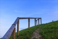Wooden handrail on the hill path, green lawn and clear blue sky. Royalty Free Stock Photo