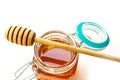 Wooden honey spoon lies on an open glass jar with floral golden honey