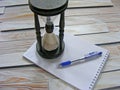 Wooden hourglass, pen and agenda on the wooden wall background Royalty Free Stock Photo