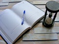 Wooden hourglass, pen and book agenda on the wooden wall background Royalty Free Stock Photo