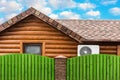 Wooden house with air conditioning, surrounded by a green fence. Blue sky with clouds Royalty Free Stock Photo