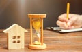 Wooden house and clock. A person signs documents. Signing a contract to rent a house or apartment. Making a will. Testament