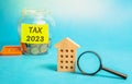 Wooden house and glass jar with money Tax 2023. The concept of paying the tax rate. Taxation, taxes burden. Pay off debts.
