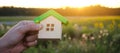 Wooden house in the hands in the sunset background. Real estate concept. Eco friendly home. Symbol of happy family life.