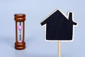 Wooden house model with blurred hourglass background. Copy space.