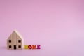 Wooden house model with HOME alphabet on pink background