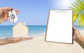 Wooden house model with key in girl hand and blank clipboard over tropical beach Royalty Free Stock Photo