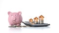 Wooden house model that is on a money stack including pink piggy bank on white background. Royalty Free Stock Photo