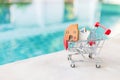 Wooden house model in shopping cart over blurred swimming pool water background Royalty Free Stock Photo